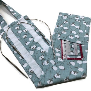 May include: A light blue fabric needle case with a white cotton flower print. The case has a pocket with a ruler and needle gauge. Two silver knitting needles are sticking out of the case.