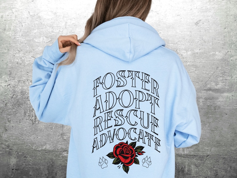 Pu&ograve; includere: Felpa con cappuccio blu chiaro con le parole "FOSTER ADOPT RESCUE ADVOCATE" in nero sul retro. Un rosa rossa con due impronte di zampa si trova sotto il testo.