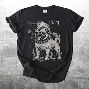 May include: Black t-shirt featuring a distressed graphic of a pug with a mohawk and studded collar. The dog is depicted in a punk rock style, with a tongue sticking out. The shirt is laid flat on a textured surface.
