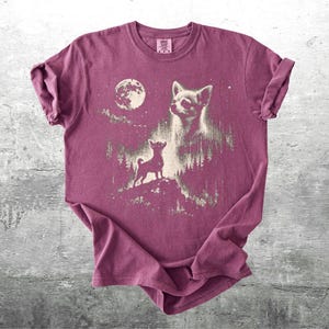 May include: A maroon t-shirt featuring a graphic of a chihuahua under a full moon. The design includes a large chihuahua head and a smaller chihuahua standing on a hill. The shirt has rolled-up sleeves and a crew neck.