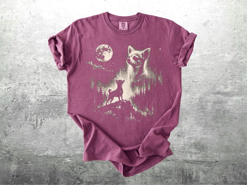 May include: A maroon t-shirt featuring a graphic of a chihuahua under a full moon. The design includes a large chihuahua head and a smaller chihuahua standing on a hill. The shirt has rolled-up sleeves and a crew neck.