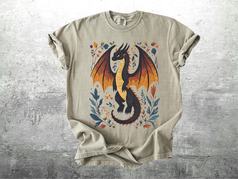 May include: A light gray t-shirt with a black dragon illustration. The dragon has orange and yellow wings and is surrounded by colorful floral designs.