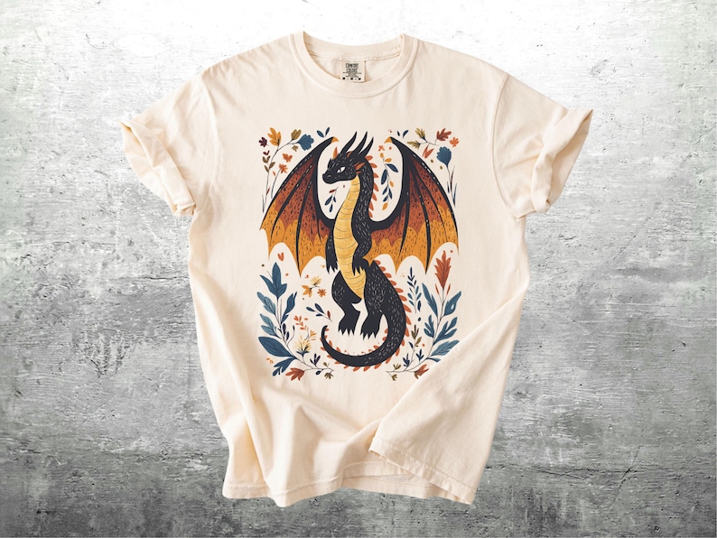 May include: A cream-colored t-shirt with a black dragon illustration. The dragon is surrounded by colorful flowers and leaves.
