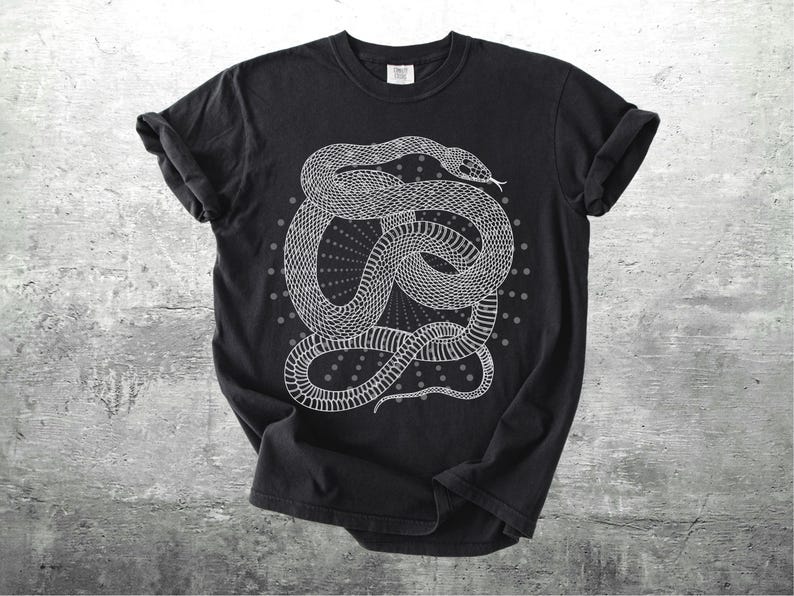 Może przedstawiać: Czarny t-shirt z białą ilustracją zwiniętego węża. Wz&oacute;r węża jest szczeg&oacute;łowy i otoczony wzorem w kropki. T-shirt ma podwinięte rękawy i okrągły dekolt. Koszulka wykonana jest z miękkiego materiału.