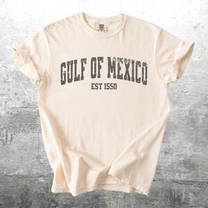 May include: A cream colored t-shirt with a distressed black graphic that reads "GULF OF MEXICO EST 1550".