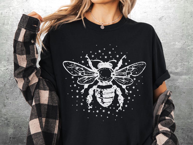 May include: Black crew neck t-shirt featuring a white graphic of a bee with detailed wings and body, surrounded by small stars. The shirt has short sleeves and a relaxed fit, suitable for casual wear.