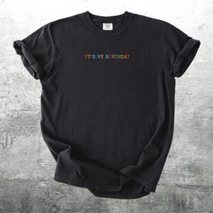 Puede incluir: Camiseta negra con el texto "IT'S MY BIRTHDAY" en colores arco&iacute;ris.