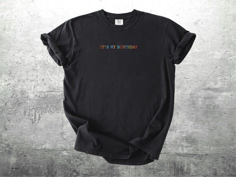 Puede incluir: Camiseta negra con el texto "IT'S MY BIRTHDAY" en colores arco&iacute;ris.