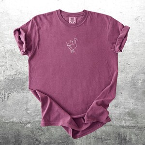 May include: A maroon t-shirt with a white outline of a goose and the word "Silly" above it.