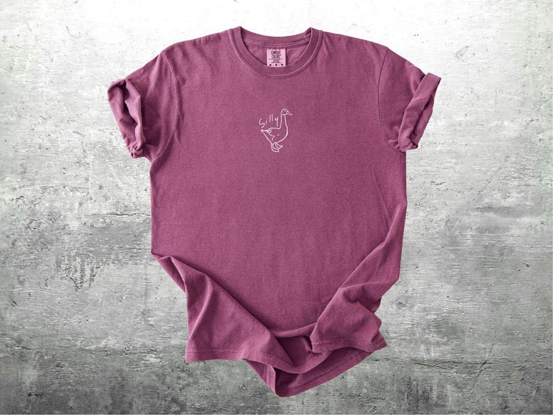 May include: A maroon t-shirt with a white outline of a goose and the word "Silly" above it.