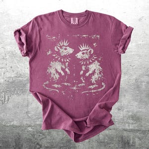 K&ouml;nnte beinhalten: Burgunderfarbenes T-Shirt mit einem Used-Look-Motiv von zwei Ratten mit Kronen und Stachelhalsb&auml;ndern. Die Ratten blicken sich an. Das T-Shirt hat hochgekrempelte &Auml;rmel und ein kleines Etikett am Ausschnitt.