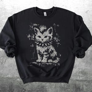 May include: Black sweatshirt featuring a distressed graphic of a punk rock kitten with a spiked collar. The cat has a mohawk and a stern expression. The design is in shades of gray and white, contrasting against the black fabric.