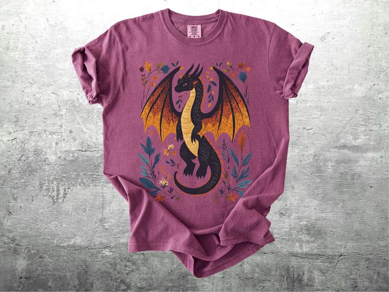 May include: A maroon t-shirt with a black and orange dragon illustration. The dragon is surrounded by floral designs in shades of yellow, orange, and green.
