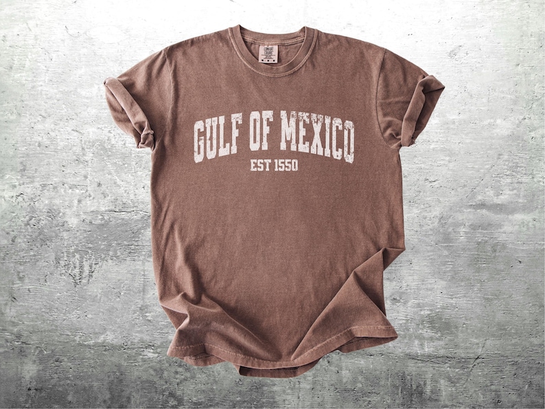 May include: A brown t-shirt with the text "GULF OF MEXICO EST 1550" printed in white.