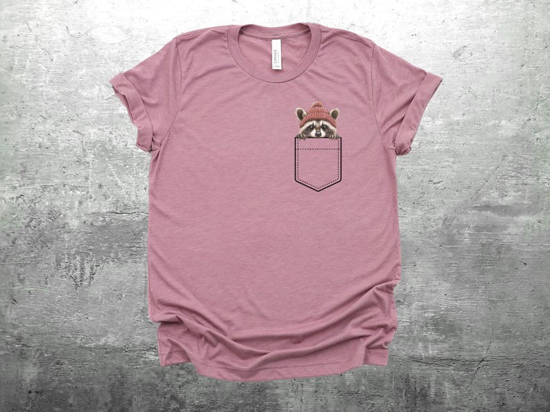 May include: A pink t-shirt with a raccoon wearing a red knit hat in the pocket.