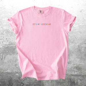 Puede incluir: Camiseta rosa con el texto "IT'S MY BIRTHDAY" en colores arco&iacute;ris.
