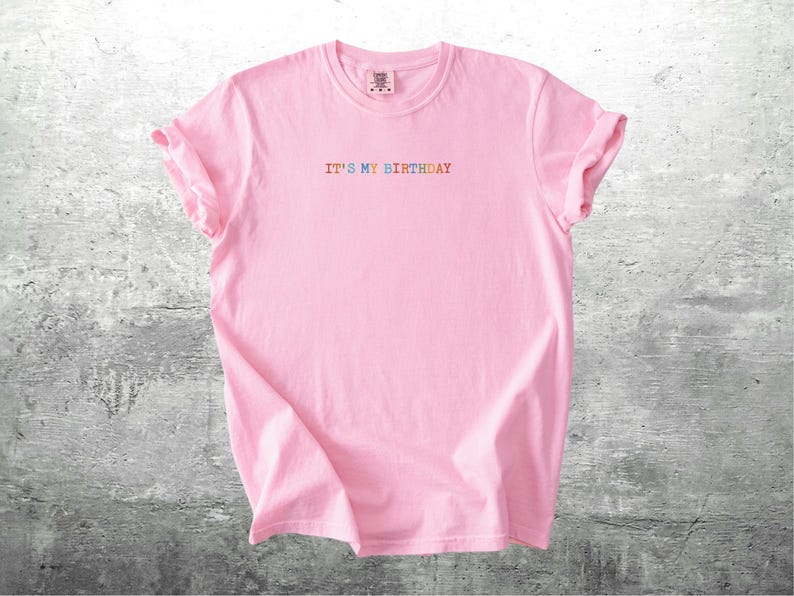 Puede incluir: Camiseta rosa con el texto "IT'S MY BIRTHDAY" en colores arco&iacute;ris.