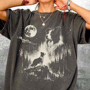 Pu&ograve; includere: T-shirt grigio scuro con una grafica in bianco e nero di un cane Border Collie, una luna piena e una scena di foresta. Il design ha un aspetto vintage e usurato. La t-shirt ha maniche corte e una vestibilit&agrave; ampia.