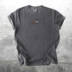 May include: Charcoal grey t-shirt with rolled sleeves. The shirt has an embroidered design of a donkey and a barrel, with the text "I don't give a". The fabric has a soft, textured appearance.
