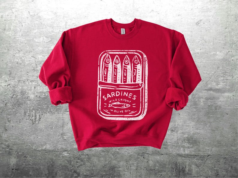 May include: A red sweatshirt with a white graphic of a sardine can. The can contains four fish and the words "Sardines Wild Caught in Olive Oil". The sweatshirt has cuffed sleeves.