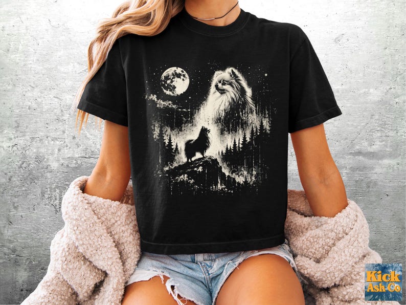 May include: A black short-sleeve t-shirt featuring a white graphic print of a fluffy Pomeranian dog standing on a rocky cliff in a forest at night. The design includes a large full moon, starry sky, and a ghostly, ethereal image of the dog's face.