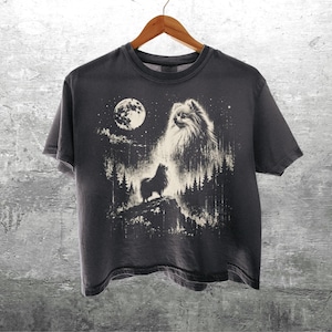 May include: A dark gray short-sleeve t-shirt featuring a graphic print of a fluffy dog standing on a rocky cliff in a forest at night under a full moon. The design includes a large ghostly dog face in the sky above the trees and the text Kick Ash-Co.