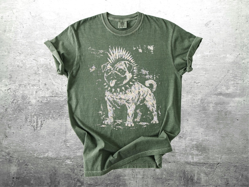 May include: Olive green t-shirt featuring a distressed graphic of a pug with a mohawk and studded collar. The dog's tongue is sticking out. The shirt has rolled-up sleeves and a crew neck.