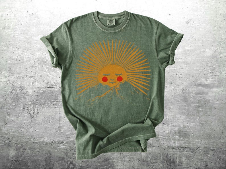 K&ouml;nnte beinhalten: Gr&uuml;nes T-Shirt mit einem Sonnengrafik. Die Sonne hat orangefarbene Strahlen, ein l&auml;chelndes Gesicht und rote Wangen &uuml;ber einer Bergkette. Das T-Shirt hat einen Vintage-Look und hochgekrempelte &Auml;rmel. Das Design ist mittig auf der Vorderseite.