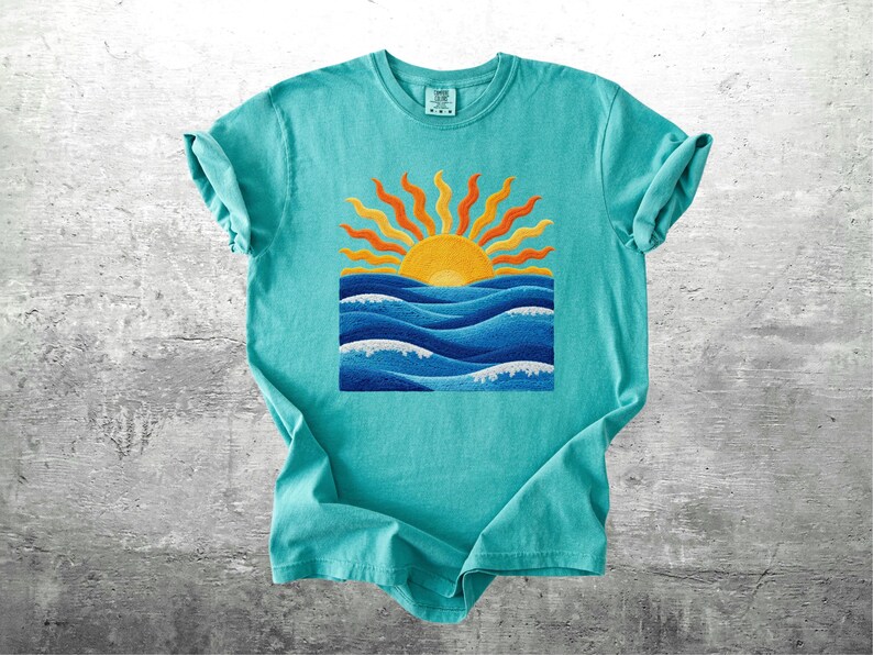 May include: A turquoise t-shirt featuring a vibrant graphic of a yellow sun with orange rays above blue ocean waves. The design is centered on the shirt, creating a summery and cheerful aesthetic. The shirt has short sleeves and a crew neck.