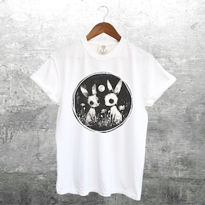 Op de afbeelding: Wit T-shirt met een zwart-witte grafische print van twee konijnen in een cirkel met een maan en sterren. De konijnen zijn gestileerd en hebben grote ogen.