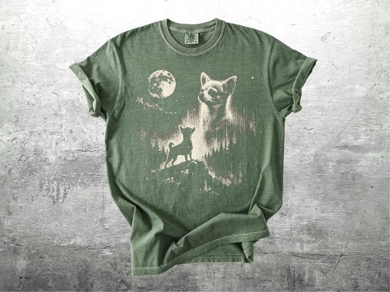 May include: Green t-shirt featuring a graphic of a Chihuahua dog under a full moon. The design includes a silhouette of the dog on a hill and a larger image of the dog's face. The shirt has a vintage, distressed look.