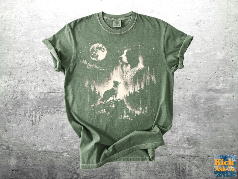 Pu&ograve; includere: T-shirt verde con una grafica di un cane in una foresta sotto la luna piena. Il design &egrave; in tonalit&agrave; di bianco e beige, con la silhouette del cane e i dettagli della foresta. La maglietta ha le maniche arrotolate.