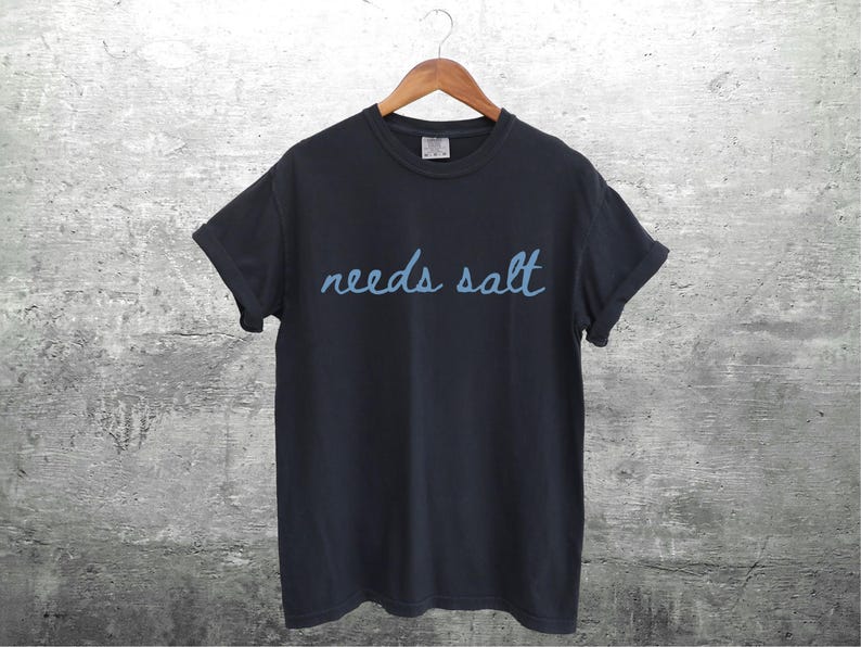 May include: A black t-shirt with the text "needs salt" written in blue cursive.