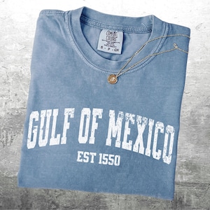 May include: A light blue t-shirt with a white distressed graphic that reads "GULF OF MEXICO EST 1550".