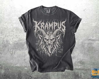 Op de afbeelding: Een antracietgrijs t-shirt met korte mouwen en een verweerde witte afbeelding van de gehoornde figuur Krampus met een lange tong. Het woord KRAMPUS staat in een gestileerd, grillig lettertype boven het hoofd op de borst.