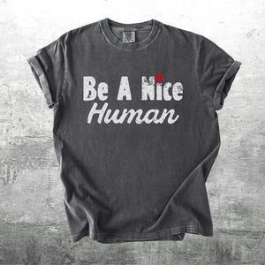 K&ouml;nnte beinhalten: Dunkelgraues T-Shirt mit hochgekrempelten &Auml;rmeln. Das Shirt zeigt den Text "Be A Nice Human" in Wei&szlig;, mit einem kleinen roten Herz &uuml;ber dem Wort "Nice".
