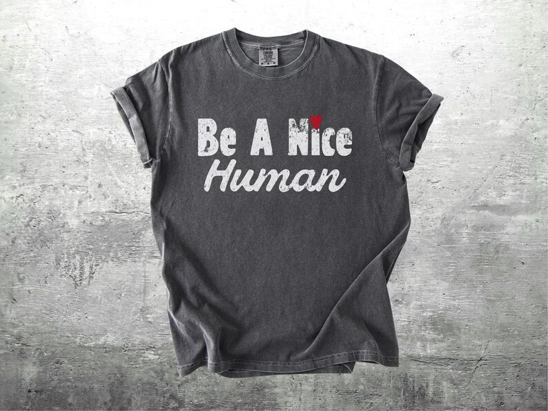 K&ouml;nnte beinhalten: Dunkelgraues T-Shirt mit hochgekrempelten &Auml;rmeln. Das Shirt zeigt den Text "Be A Nice Human" in Wei&szlig;, mit einem kleinen roten Herz &uuml;ber dem Wort "Nice".