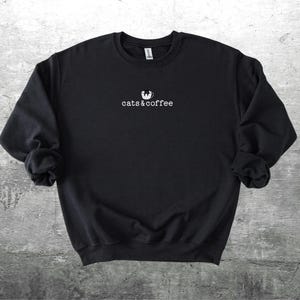 May include: Black sweatshirt with the text "cats & coffee" in white, with a cat silhouette above the text. The sweatshirt is made of a soft material and has long sleeves.