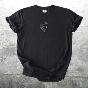 May include: Black t-shirt with a white outline of a goose and the word "Silly" above it.