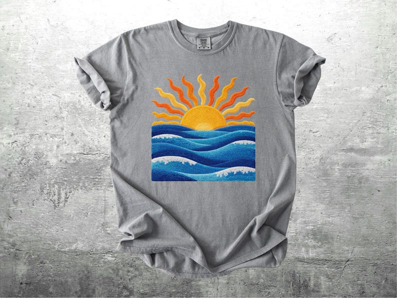 May include: A gray t-shirt featuring a vibrant graphic of a sunset over ocean waves. The sun is yellow and orange, with blue waves and white foam. The shirt is made of soft material.