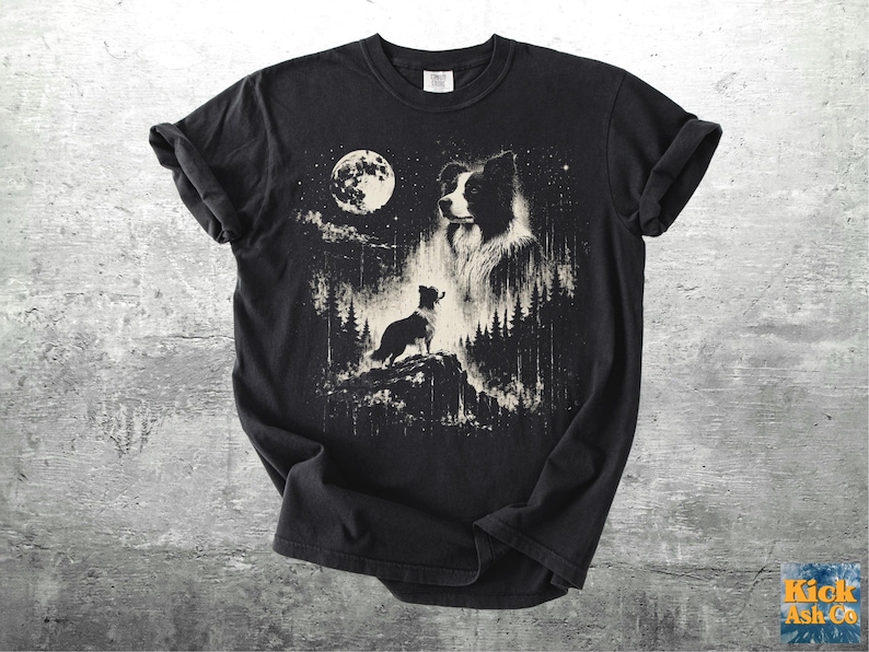 Pu&ograve; includere: T-shirt nero con una grafica dettagliata di un cane Border Collie sotto la luna piena. Il design include una silhouette di cane su una collina, alberi e stelle, creando una scena notturna.