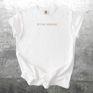 Puede incluir: Camiseta blanca con el texto "IT'S MY BIRTHDAY" en colores arco&iacute;ris.
