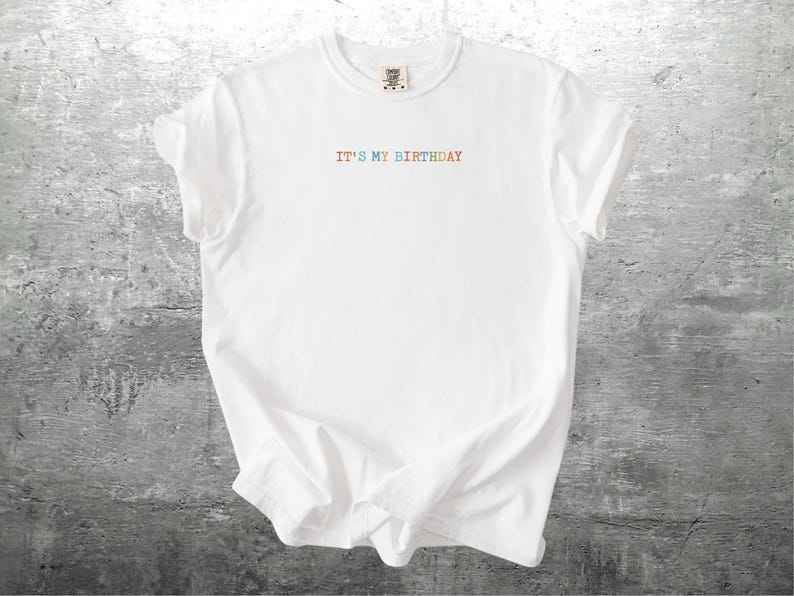 Puede incluir: Camiseta blanca con el texto "IT'S MY BIRTHDAY" en colores arco&iacute;ris.
