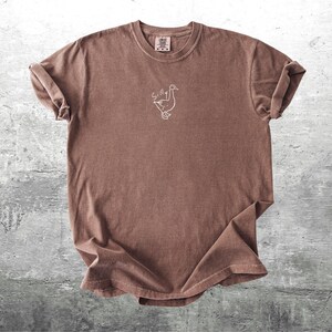 May include: A brown t-shirt with a white outline of a goose and the word "Silly" above it.