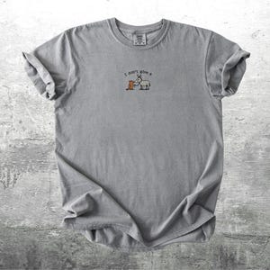 May include: A grey t-shirt with rolled sleeves. The shirt has a small graphic of a donkey and a carrot with the text "I don't give a". The t-shirt is made of a soft material and is suitable for casual wear.