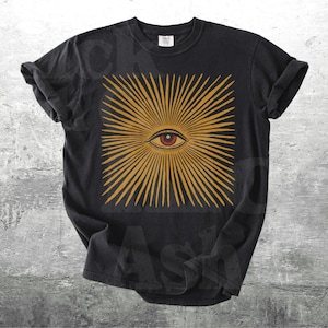 May include: Black t-shirt featuring a square design with a central eye and radiating golden lines. The eye is red and the design is centered on the shirt. The shirt is a classic crew neck style.
