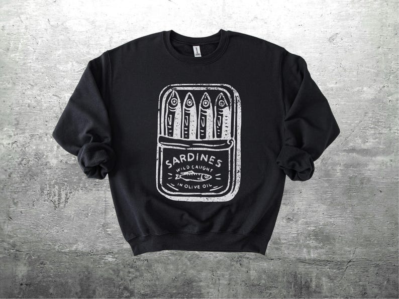 May include: Black sweatshirt with a white graphic of a sardine can. The can contains four sardines and the text "Sardines Wild Caught in Olive Oil". The design has a vintage, hand-drawn aesthetic.