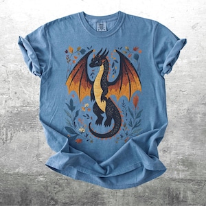 May include: A blue t-shirt with a black dragon illustration. The dragon has orange and yellow wings and is surrounded by floral designs.