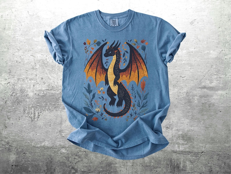 May include: A blue t-shirt with a black dragon illustration. The dragon has orange and yellow wings and is surrounded by floral designs.