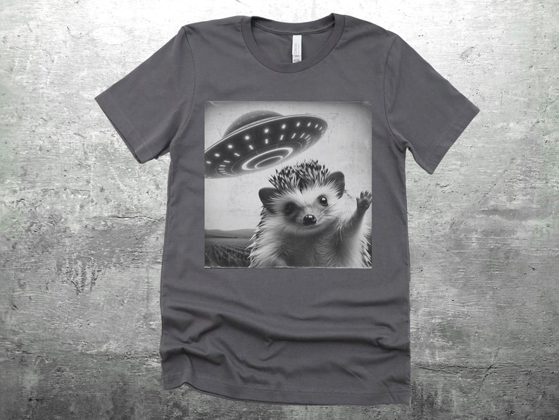 May include: A dark gray t-shirt with a black and white image of a hedgehog waving at a flying saucer.